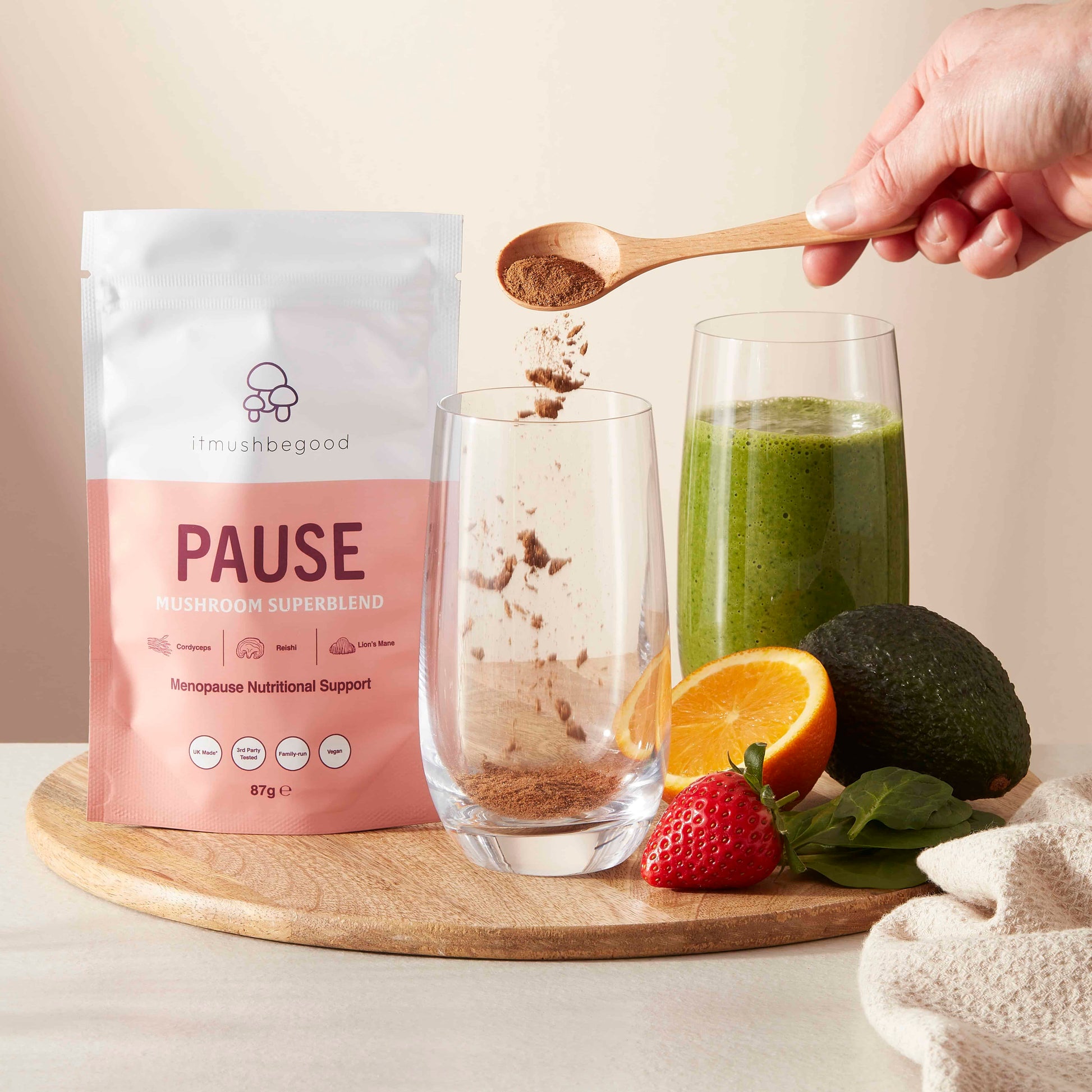 Pause supplement being spooned into a glass with smoothie and fruits on a wooden board